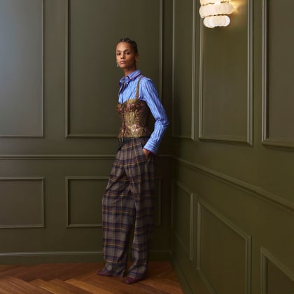 Model wearing a blue striped shirt layered with a patterned corset and checked trousers.