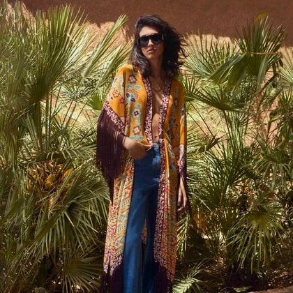 Model wearing a colorful Etro Summer capsule kimono with fringe details, styled with wide-leg jeans and sunglasses.