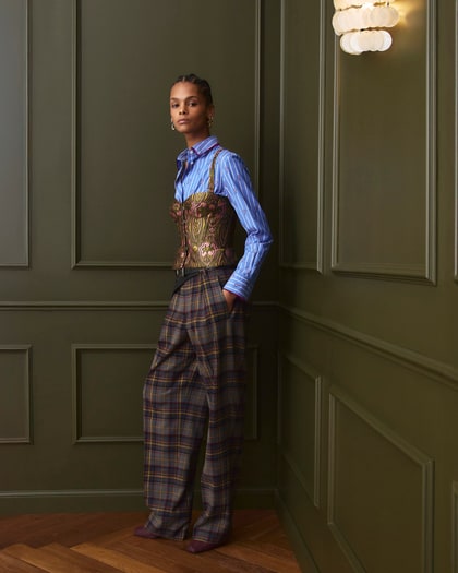 Model wearing a blue striped shirt layered with a patterned corset and checked trousers.