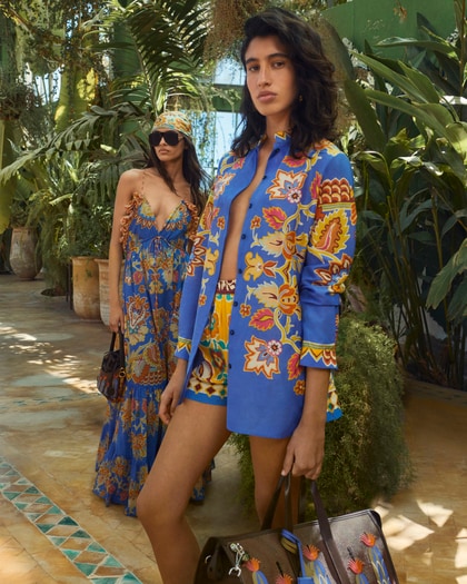 Two models wearing vibrant, floral-patterned Etro resortwear in a lush, tropical setting.