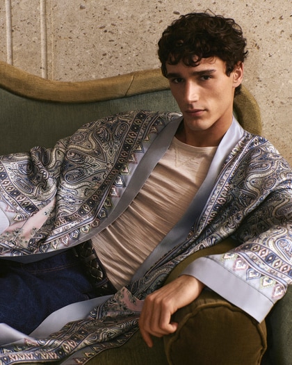 Model wearing an Etro patterned robe-style jacket over a T-shirt, seated indoors.