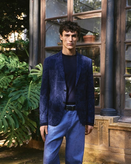 Model wearing a patterned navy Etro blazer with matching trousers, styled with a dark crewneck top in a garden setting.