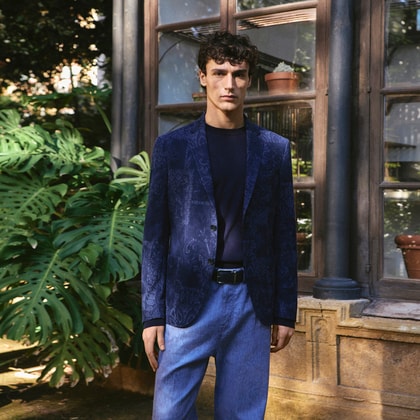 Model wearing a patterned navy Etro blazer with matching trousers, styled with a dark crewneck top in a garden setting.