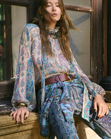 Woman wearing an Etro paisley-print dress, seated outdoors by a window.