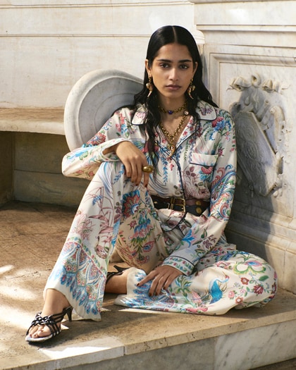 Model wearing an Etro paisley shirt and matching trousers, seated outdoors.