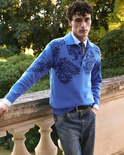 Man wearing an Etro blue patterned knit top, standing by a garden balustrade.