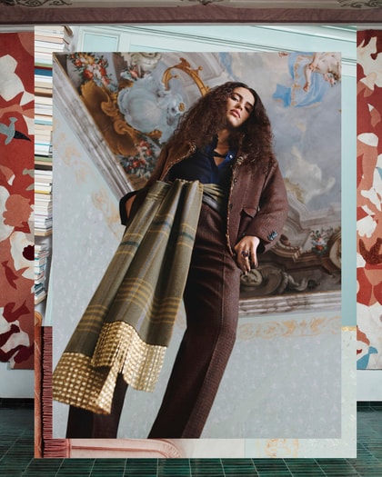 Model wearing Etro in a richly decorated interior, with a draped plaid scarf and tailored brown ensemble.