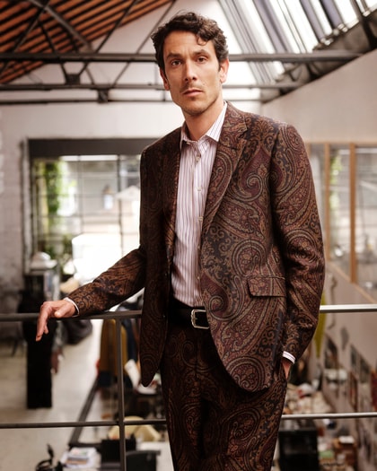 Man wearing a paisley jacket and striped shirt in a modern studio.