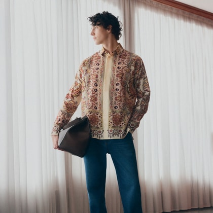 Model wearing an Etro paisley-print shirt paired with classic blue jeans, styled with a leather clutch and casual sneakers.