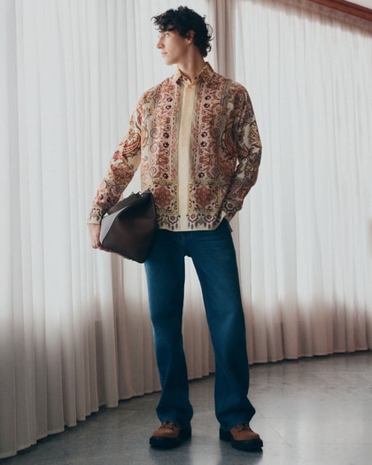 Model wearing an Etro paisley-print shirt paired with classic blue jeans, styled with a leather clutch and casual sneakers.