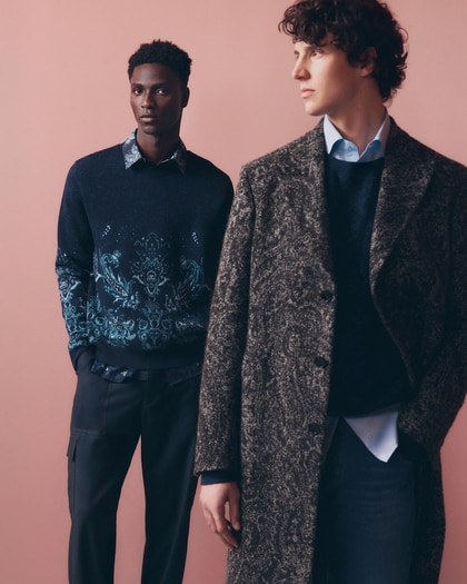 Two male models wearing patterned Etro knitwear and tailored outerwear against a pink background