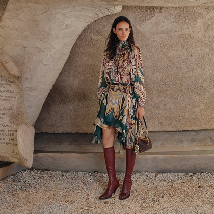 Model in a Etro silk blouse and skirt holding a brown suede Vela bag