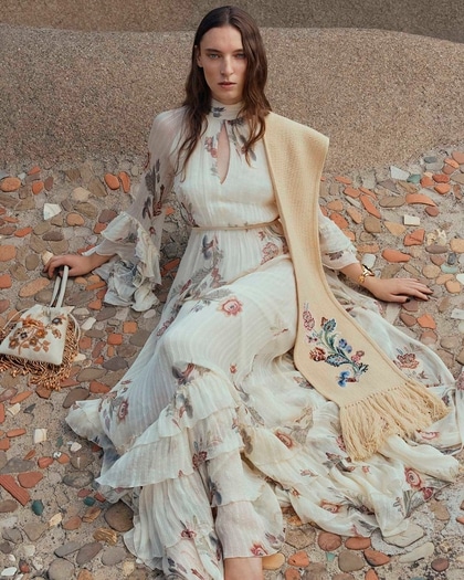 Model wearing an Etro flowing floral maxi dress with ruffled sleeves, styled with an embroidered scarf and matching handbag.