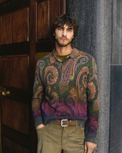 Model wearing a multicoloured paisley knit sweater with corduroy trousers, standing by a wooden doorway.