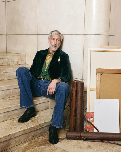 Man wearing an Etro velvet jacket, patterned shirt and jeans, seated on a marble staircase.