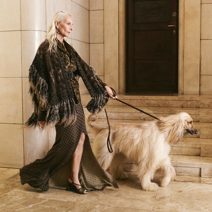 Woman wearing an Etro fringed jacket and patterned dress, walking a dog on a marble staircase.