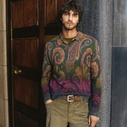Model wearing a multicoloured paisley knit sweater with corduroy trousers, standing by a wooden doorway.