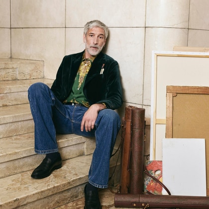 Man wearing an Etro velvet jacket, patterned shirt and jeans, seated on a marble staircase.