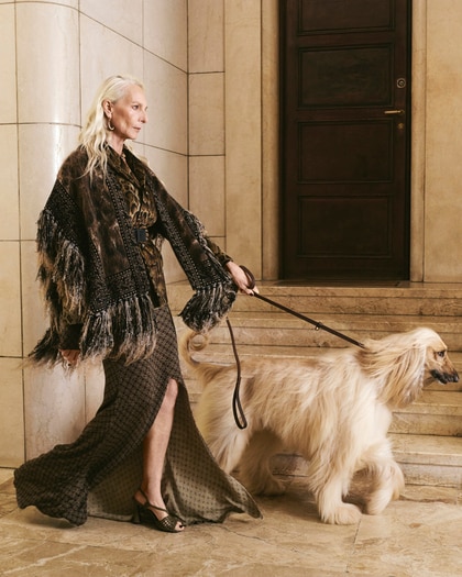 Woman wearing an Etro fringed jacket and patterned dress, walking a dog on a marble staircase.