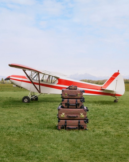 ETRO x Globe-Trotter suitcases displayed in front of an aircraft, featuring patterned trolley luggage in Etro Arnica with black detailing.