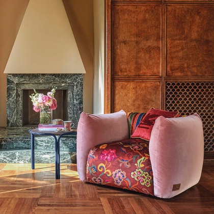 Etro Armchair with pink velvet upholstery and floral fabric near a fireplace and side table.