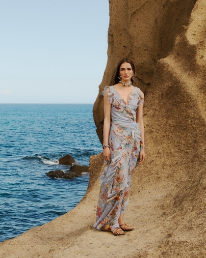 Model wearing an ETRO denim look standing outdoors by the sea next to a vintage vehicle.