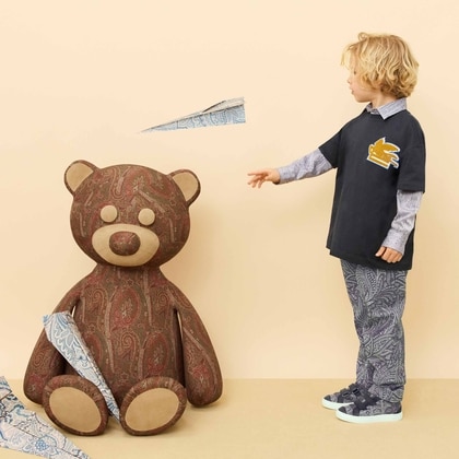 Young boy wearing an Etro outfit with a printed shirt and pants, standing beside a large paisley teddy bear.