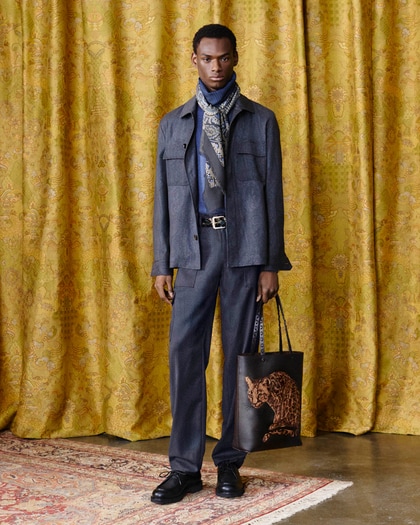 Model wearing a dark jacket with coordinated dark trousers, holding a bag with a printed animal