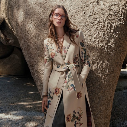 Model in a Etro trench with floral print, standing in front of a stone wall