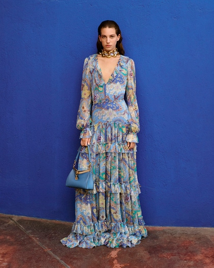 Model in a flowing, floral Etro dress with ruffles, accessorized with a blue bag and gold choker.